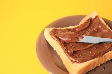 Spreading chocolate paste onto bread on yellow background, closeup. Space for text