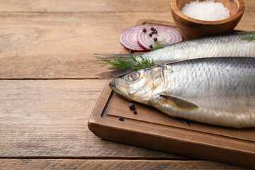 Board with delicious salted herrings, dill, onion and salt on wooden table. Space for text