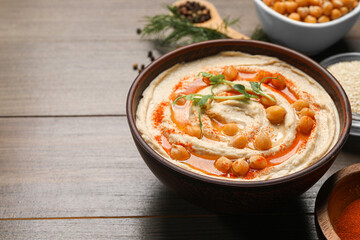 Delicious hummus with chickpeas and different ingredients on wooden table. Space for text