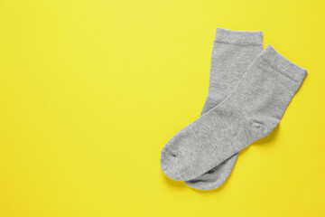 Pair of grey socks on yellow background, flat lay. Space for text