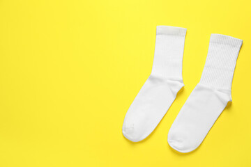 Pair of white socks on yellow background, flat lay. Space for text