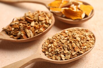 Spoons with dried orange seasoning zest and peel on beige textured table, closeup