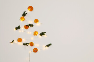 Christmas decor made of dry orange slices, festive lights and fir tree branches on white wall. Space for text