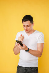 handsome young man holding a phone in his hand, talking emotionally on the phone on a yellow plain background.