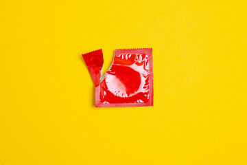 torn pack of a condom lies on a yellow background, the concept of safe sex