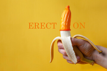 hand holds a banana with a condom, a contraceptive dressed on a sexualized banana on a yellow...
