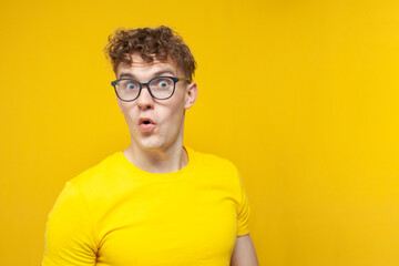 surprised guy student with curly hair holding glasses and looking at copy space, nerd in glasses on...