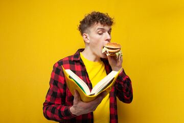 curly guy eats a big burger and reads a book on a yellow background, a student to study and eat...