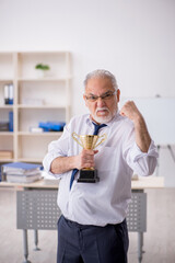 Old male employee doing sport exercises at workplace