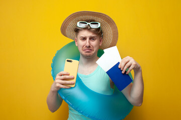 young sad guy in the summer on vacation with a passport and tickets holds a phone and cries, unhappy tourist