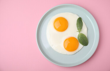 Tasty fried eggs with basil in plate on pink background, top view. Space for text
