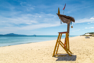A rustic life guards chair on a deserted beach under blue sky