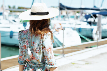 Seen from behind elegant traveller woman in floral dress on pier