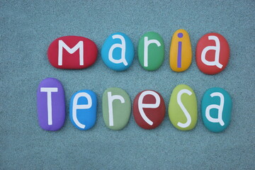 Maria Teresa, female given name composed with multi colored stone letters over green sand