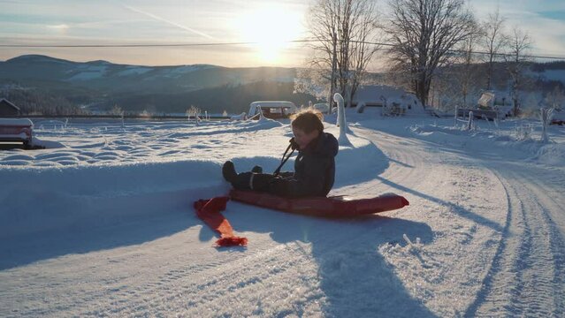 A boy is sledding in the snow during Christmas and a beautiful sunset in Norway