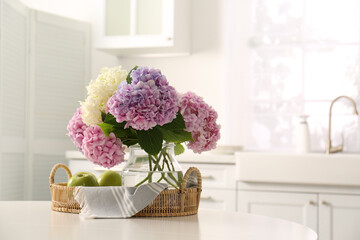 Bouquet of beautiful hydrangea flowers and apples on table in kitchen, space for text. Interior design