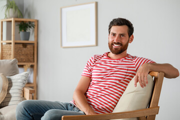 Portrait of handsome bearded man in armchair at home, space for text