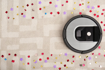 Modern robotic vacuum cleaner removing confetti from carpet, top view. Space for text
