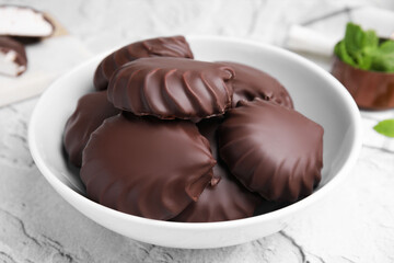 Delicious chocolate covered zephyrs in bowl on light grey table, closeup