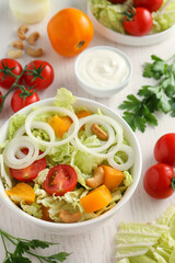 Bowl of delicious salad with Chinese cabbage and different ingredients on white wooden table