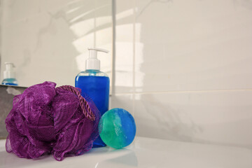 Purple shower puff and cosmetic products on sink in bathroom, space for text