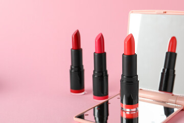 Different beautiful lipsticks and mirror on pink background, space for text