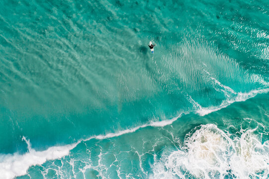 Surfers are seen from above in blue pristine ocean water