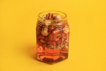 Different nuts and honey in jar on yellow background