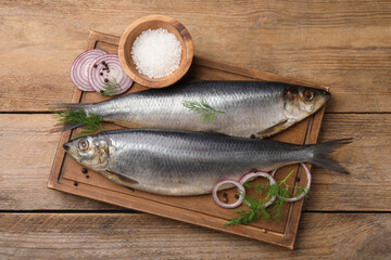Board with delicious salted herrings, dill, onion and salt on wooden table, flat lay