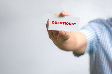 Man holding a white business card with text, Questions?
