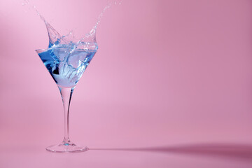 Cocktail splashing out of martini glass on pink background, space for text