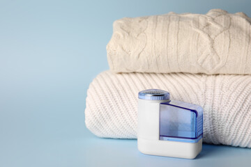 Modern fabric shaver and knitted clothes on light blue background, space for text