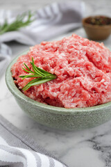 Bowl of raw fresh minced meat with rosemary on white marble table, closeup