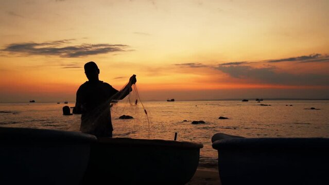 Silhouette of fisherman unloading nets at sunset on beautiful beach. Daily work to prepare for a successful sailing tomorrow morning in the central coast of Vietnam