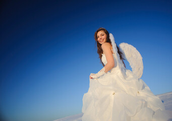 Obraz na płótnie Canvas Beautiful young woman in wedding dress walking on snow field