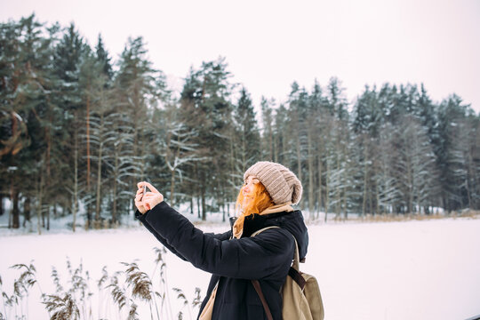 woman in winter with phone takes pictures of nature in the park on a cold day