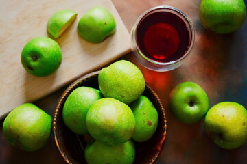 Heap of natural green apple on wooden desk and plate and slices next glass of tea. Top view, flat lay