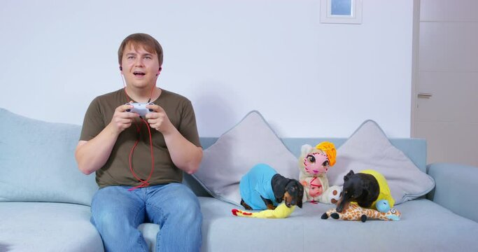 Family day off man enthusiastically plays video games in hands of joystick two dogs sit on sofa play with soft toys gnaw. Parenthood indifference lack of attention psychological trauma, game addiction