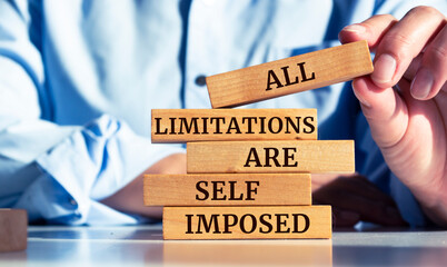 Closeup on businessman holding a wooden block with "All limitations are self imposed" message