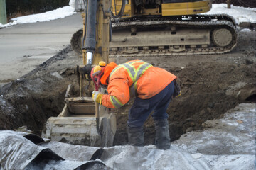 a construction worker using an excavator and a hand shovel to repair a road drain