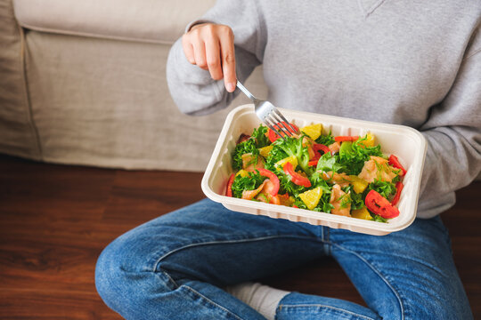 Closeup image of a woman eating salad in paper box for takeaway food at home
