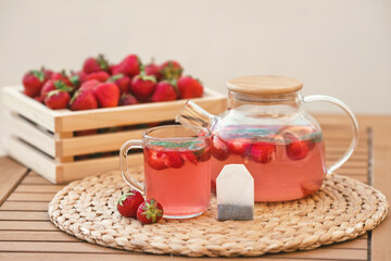 Strawberry drink from a tea bag in a cup and teapot with fresh fruits on the background of a wooden crate full of red berries