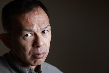 Middle-aged Japanese man in gray casual shirt on gray background. Conceptual image of world peace, stability in daily life, and sustainable living.