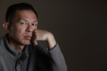 Middle-aged Japanese man in gray casual shirt on gray background. Conceptual image of world peace, stability in daily life, and sustainable living.