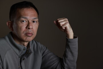 Middle-aged Japanese man in gray casual shirt on gray background. Conceptual image of world peace, stability in daily life, and sustainable living.