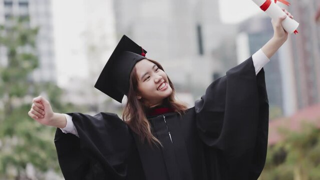 Successful graduation from university. Smiling beautiful Asian girl university or college graduate standing over university at background.
