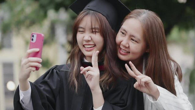 Asian mother and graduated daughter take selfie by smartphone at campus university.