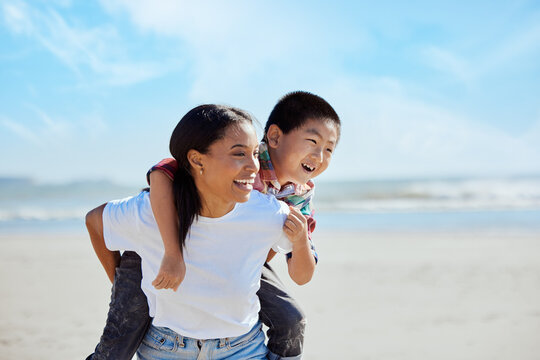 Mom, Beach Piggyback And Asian Kid With Interracial Family Bonding, Nature And Outdoor Vacation In Sunshine. Happy Family, Ride And Black Woman For Adoption, Love And Adventure By Ocean On Holiday