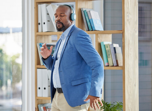 Music, dance and headphones with a business black man manager dancing in his office at work. Wellness, radio and freedom with a senior male worker listening or streaming audio while working