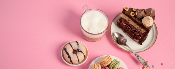 Table with various cookies, donuts, cakes, coffee cups on pink background.